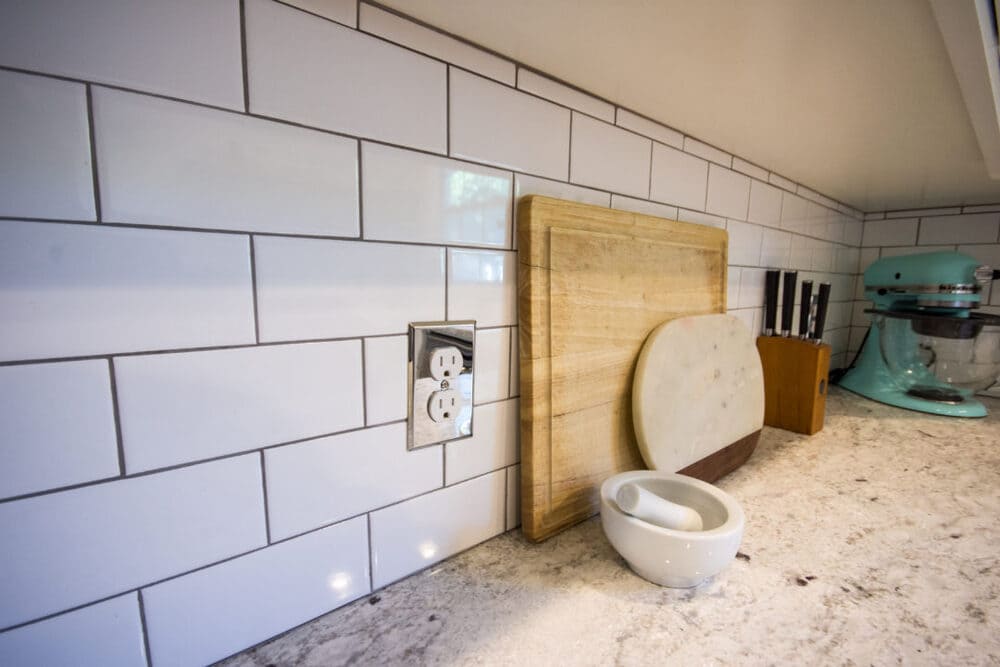 White Subway Tile Backsplash with Shiny Outlet and Wooden Cutting  Board