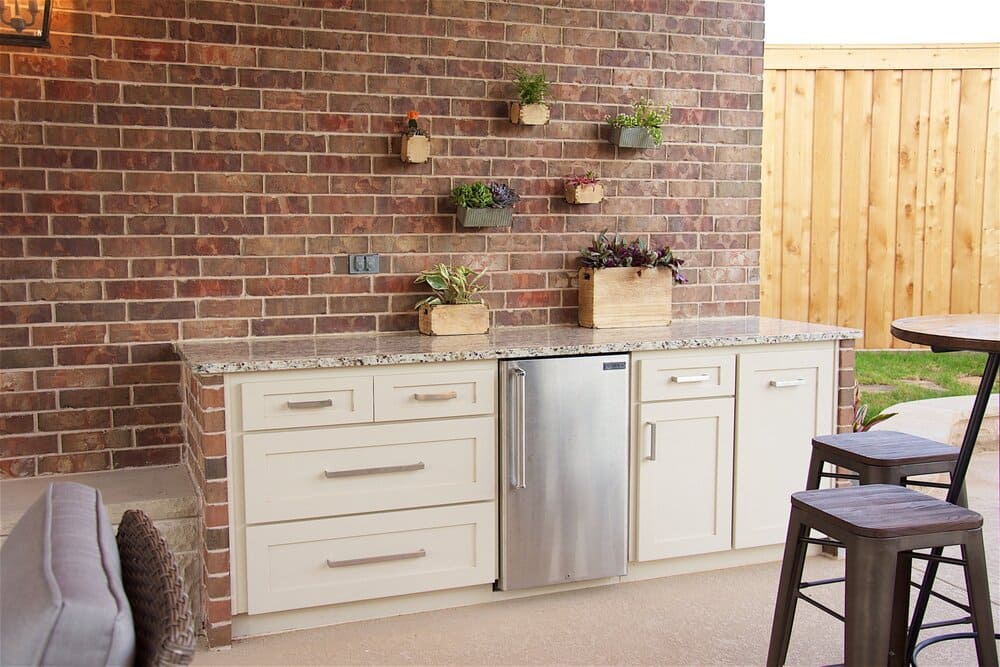 Outdoor Fridge with Wooden Chairs and Brick Backsplash