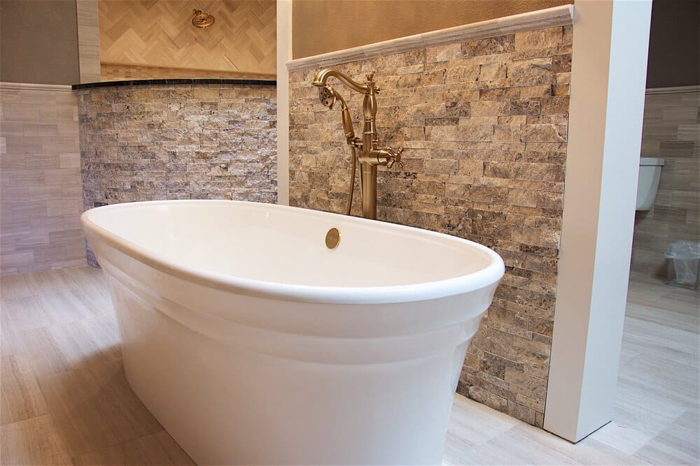 Large Bathtub Next to Rocky Brick Wall And Light Wood Floor